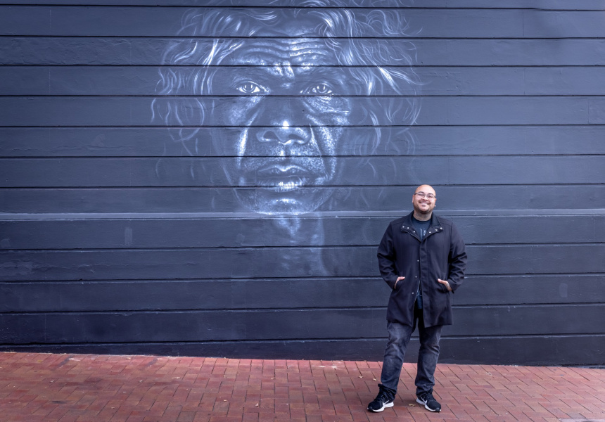 Artist Thomas Readett standing by mural of David Gulpilil
