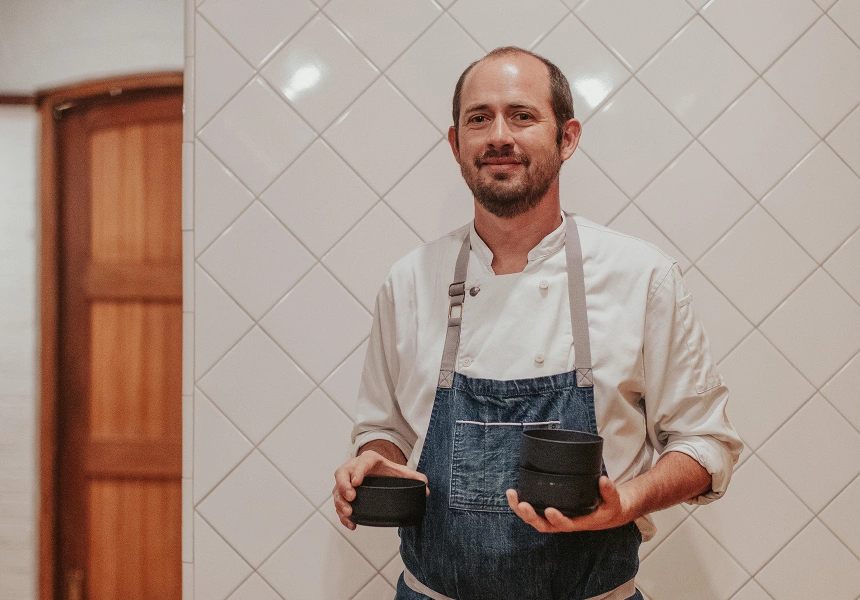 Chef Giulio Sturla stands against a white wall holding black dishes