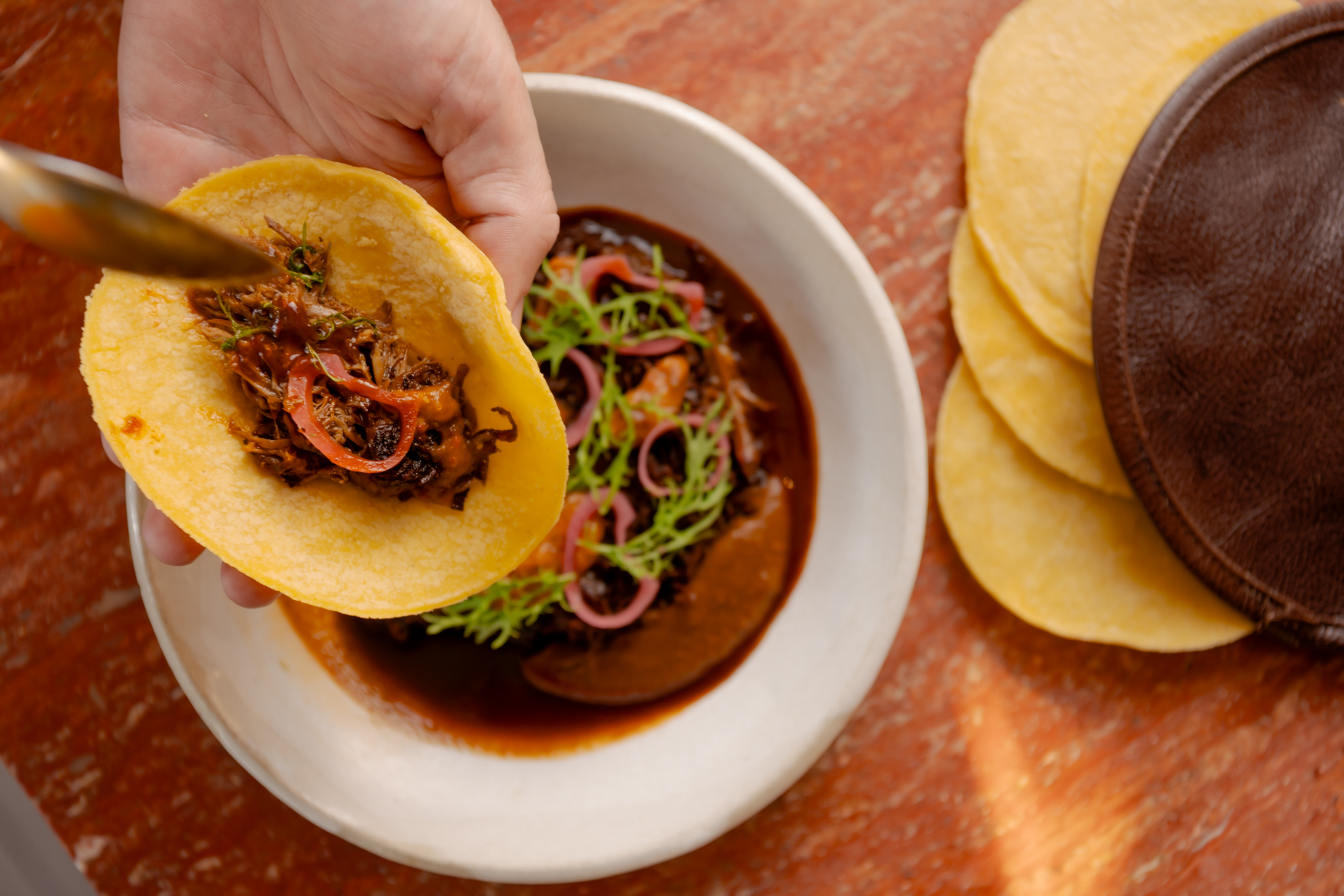 A taco being filled with goat barbacoa.